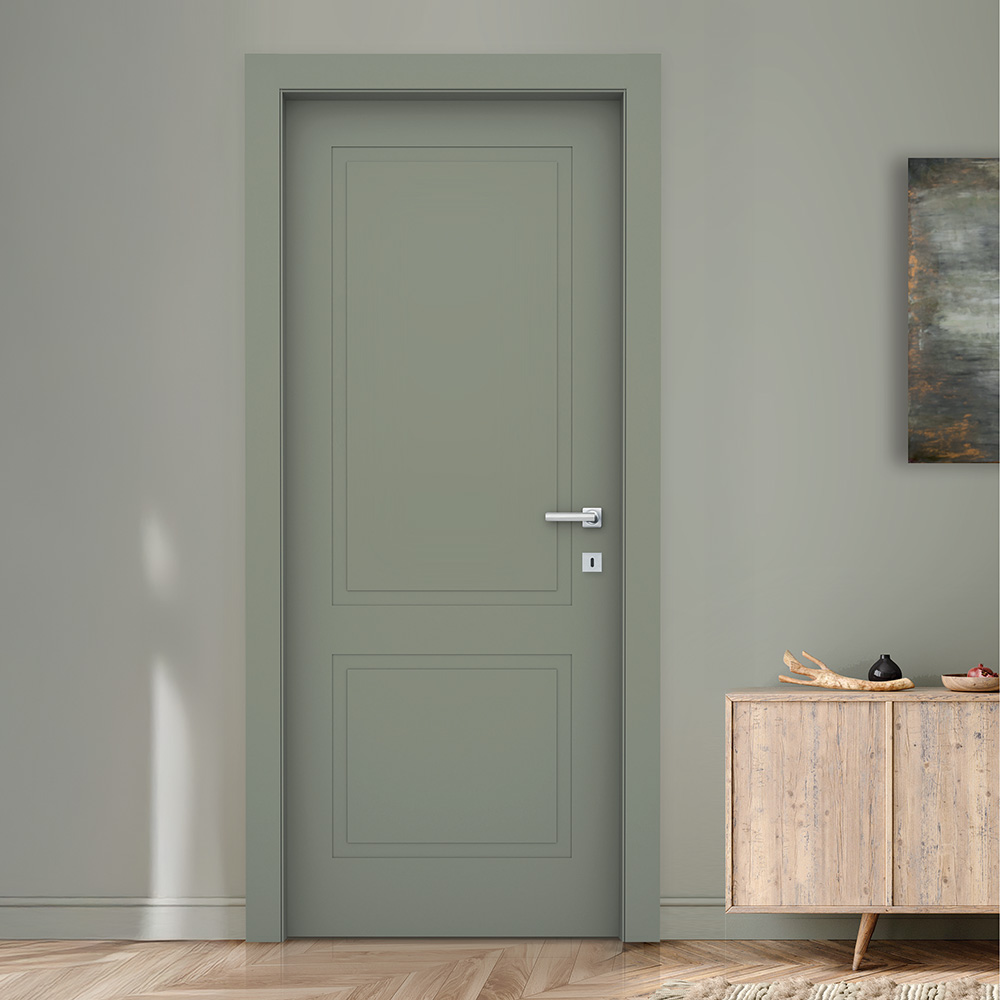 Questa immagine mostra una porta interna di colore verde salvia, con un design elegante e classico caratterizzato da due riquadri decorativi incisi. L’ambiente è raffinato, con pareti tono su tono, pavimento in parquet a spina di pesce e un mobile in legno chiaro sulla destra. Lo stile è sobrio e moderno con un tocco naturale.